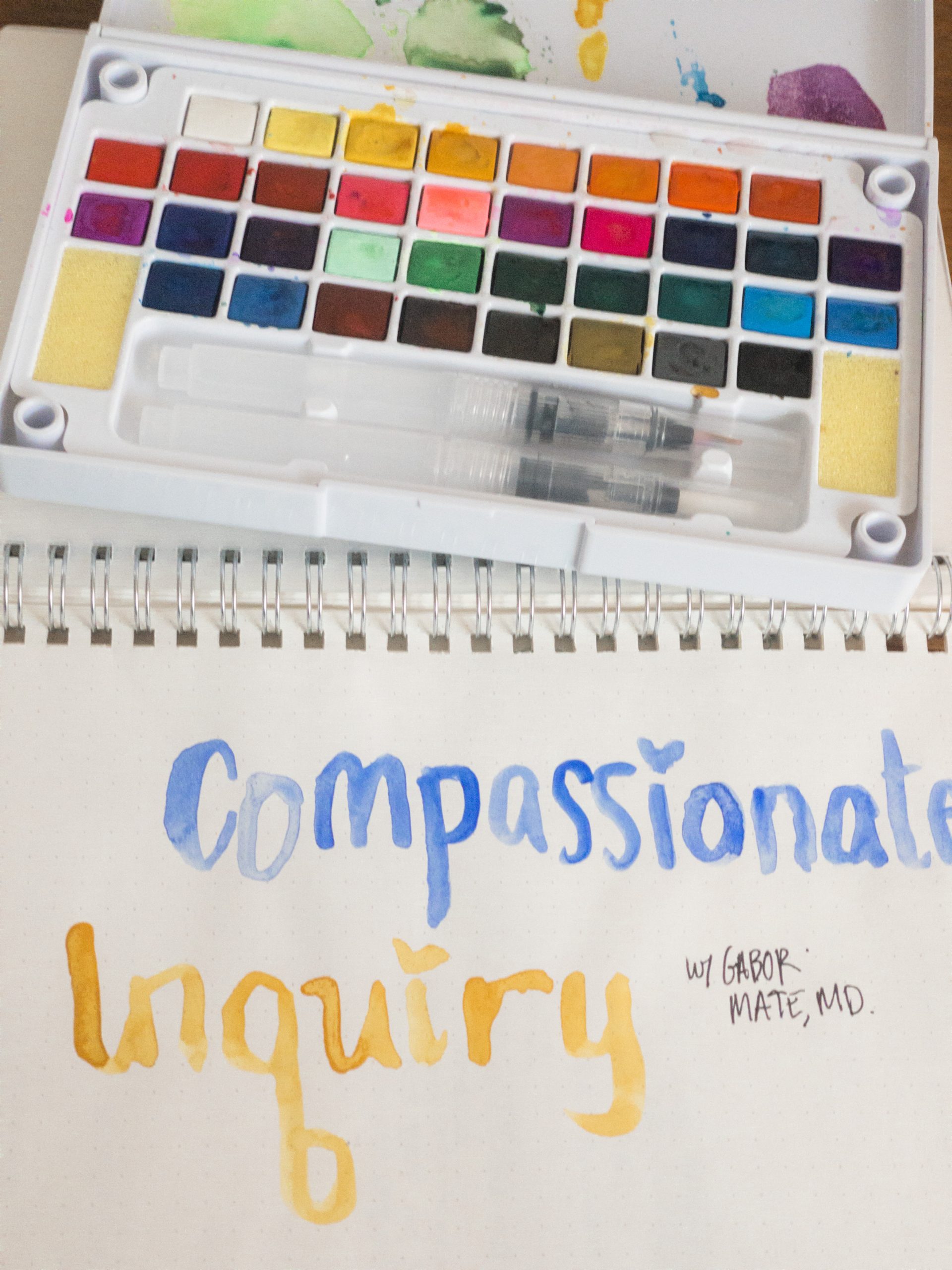 Journal with the words Compassionate Inquiry painted on it in Blue and Yellow 