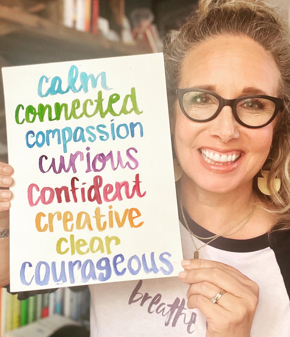 Allison holding a white piece of paper with the words calm, connected, compassionate, curious, confident, creative, clear and courageous on it.