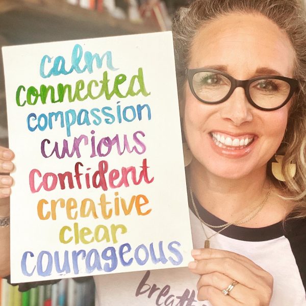 Allison holding a white piece of paper with the words calm, connected, compassionate, curious, confident, creative, clear and courageous on it.