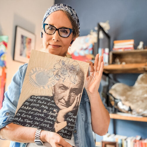 Allison holding a wood print by Sarah Bamford Seidlemann of with an image of Georgia O'Keeffe and the words ,"take time to look" painted multiple times.
